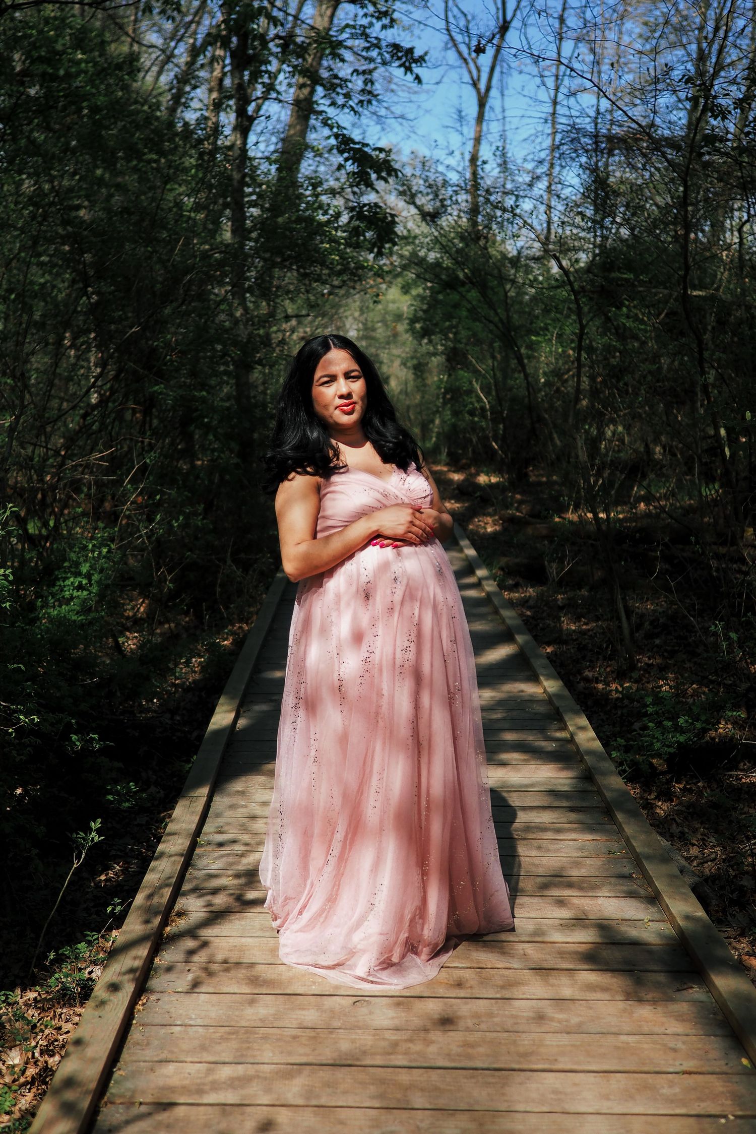 A maternity photo on a wooden boardwalk surrounded by lush forest scenery.