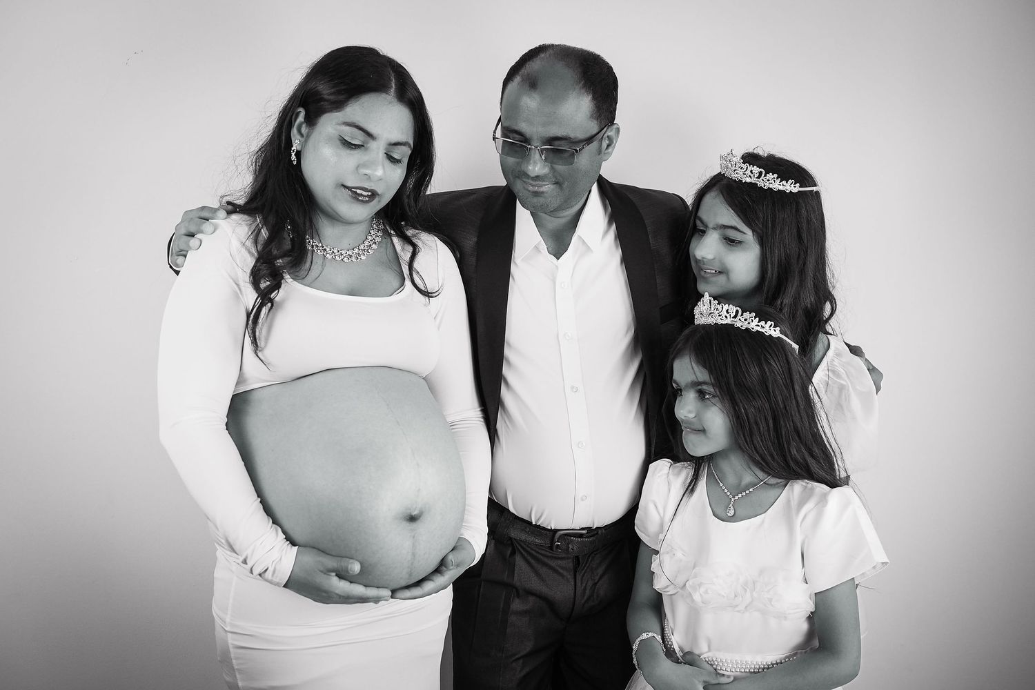 Black and white maternity portrait with family against simple background.