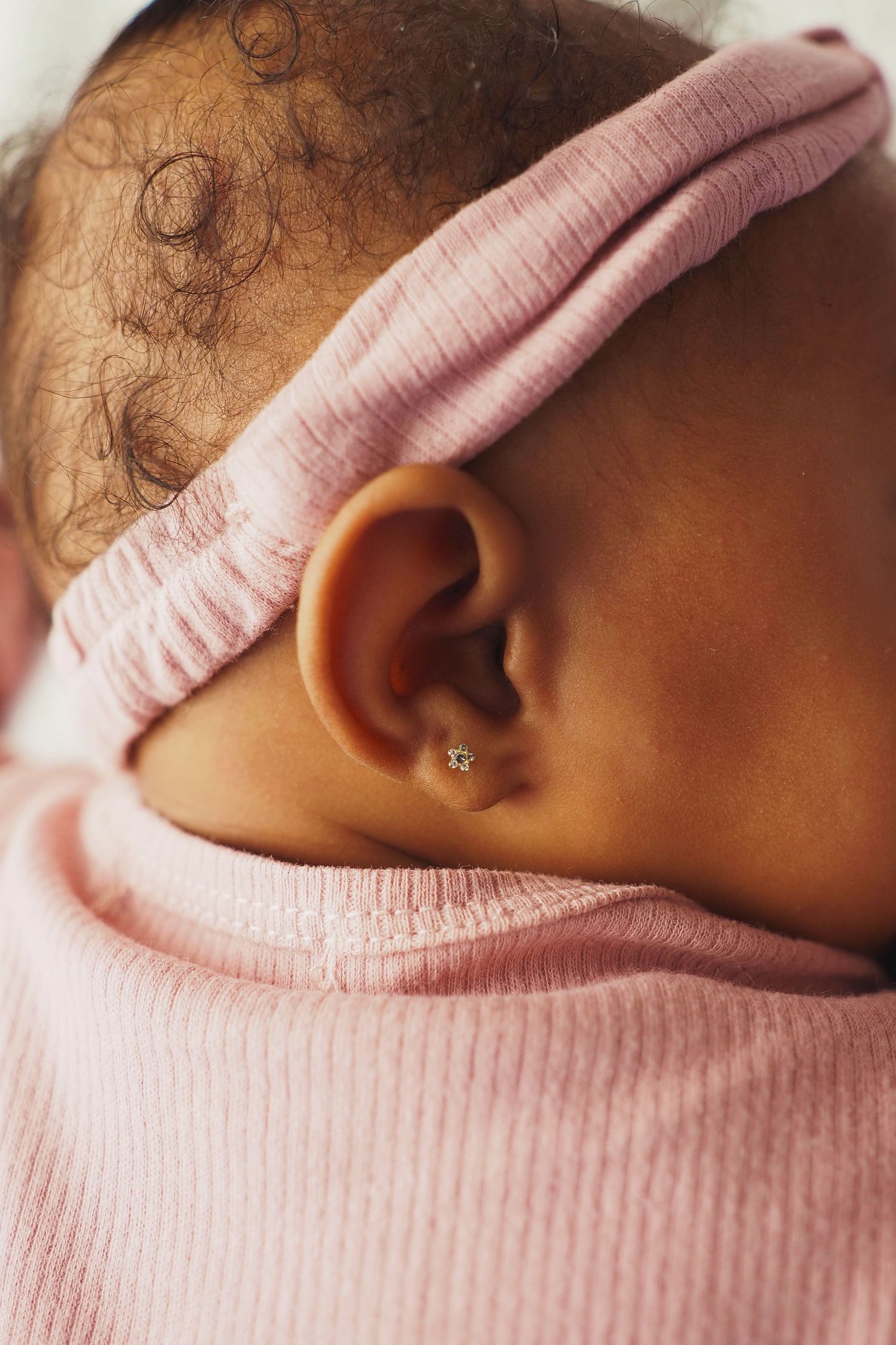 Close-up detail of a baby's ear with a pink headband and pierced earring.
