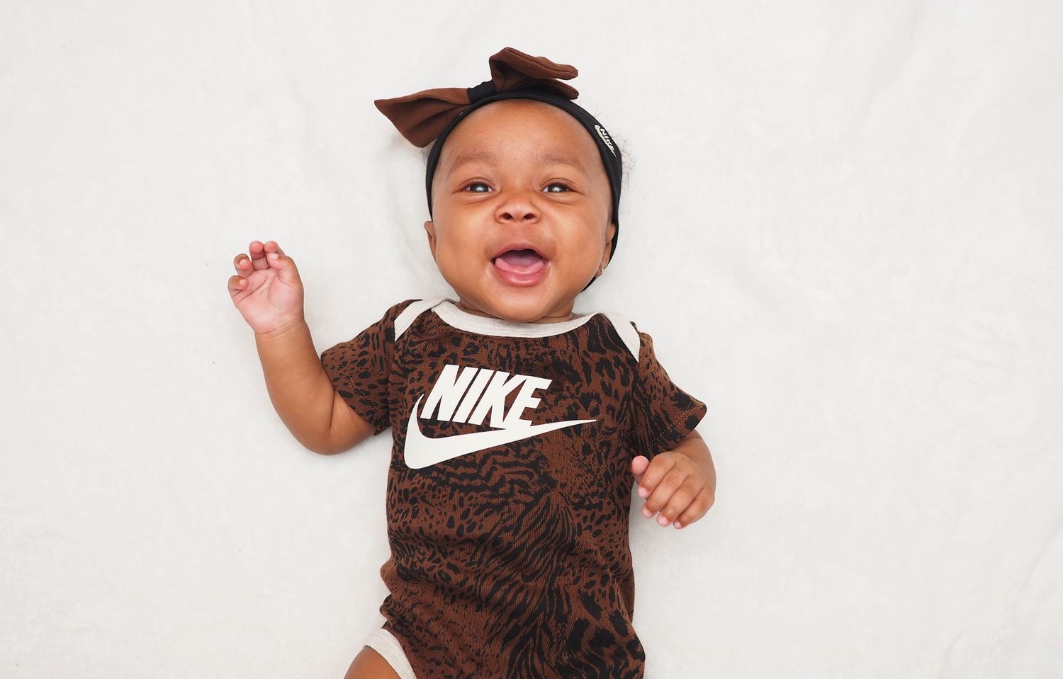 A baby wearing a brown Nike onesie and headband against a white background.