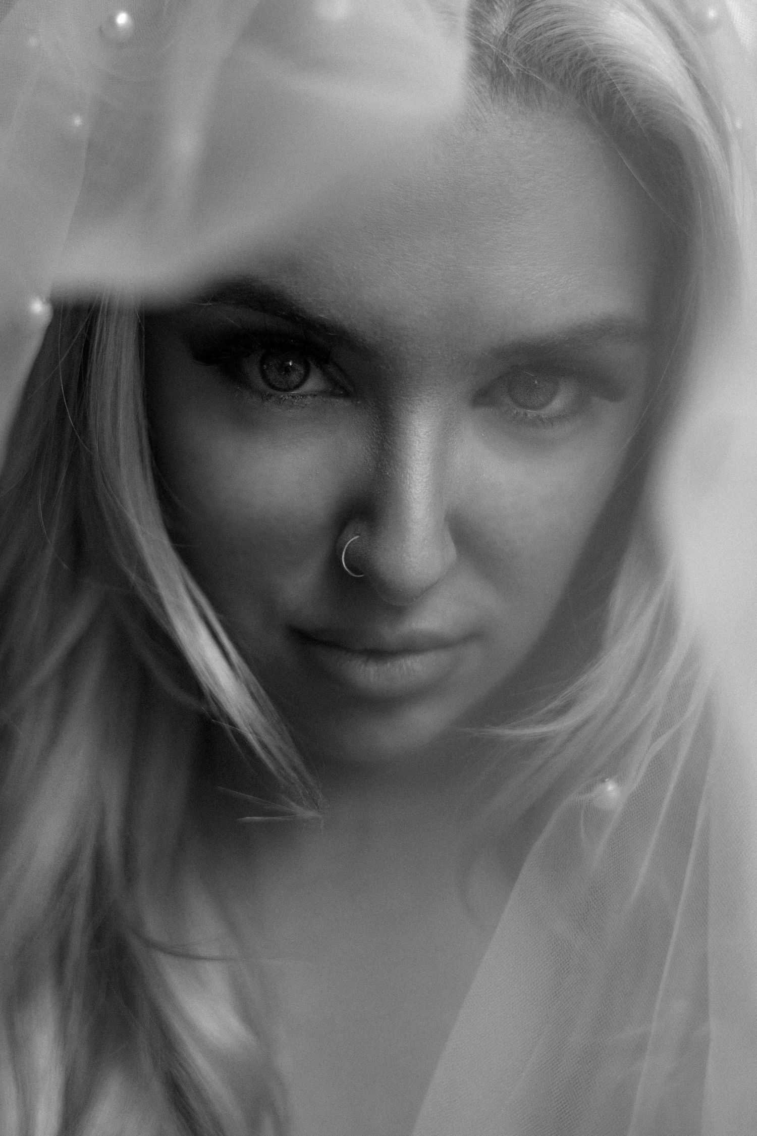 A black and white artistic portrait with soft lighting and ethereal effects shows a close-up view through a delicate veil.