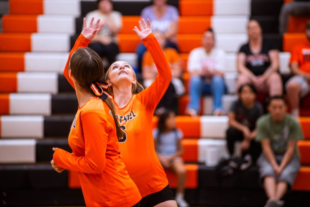 A volleyball player in orange jersey celebrates a point with arms raised during an intense match.