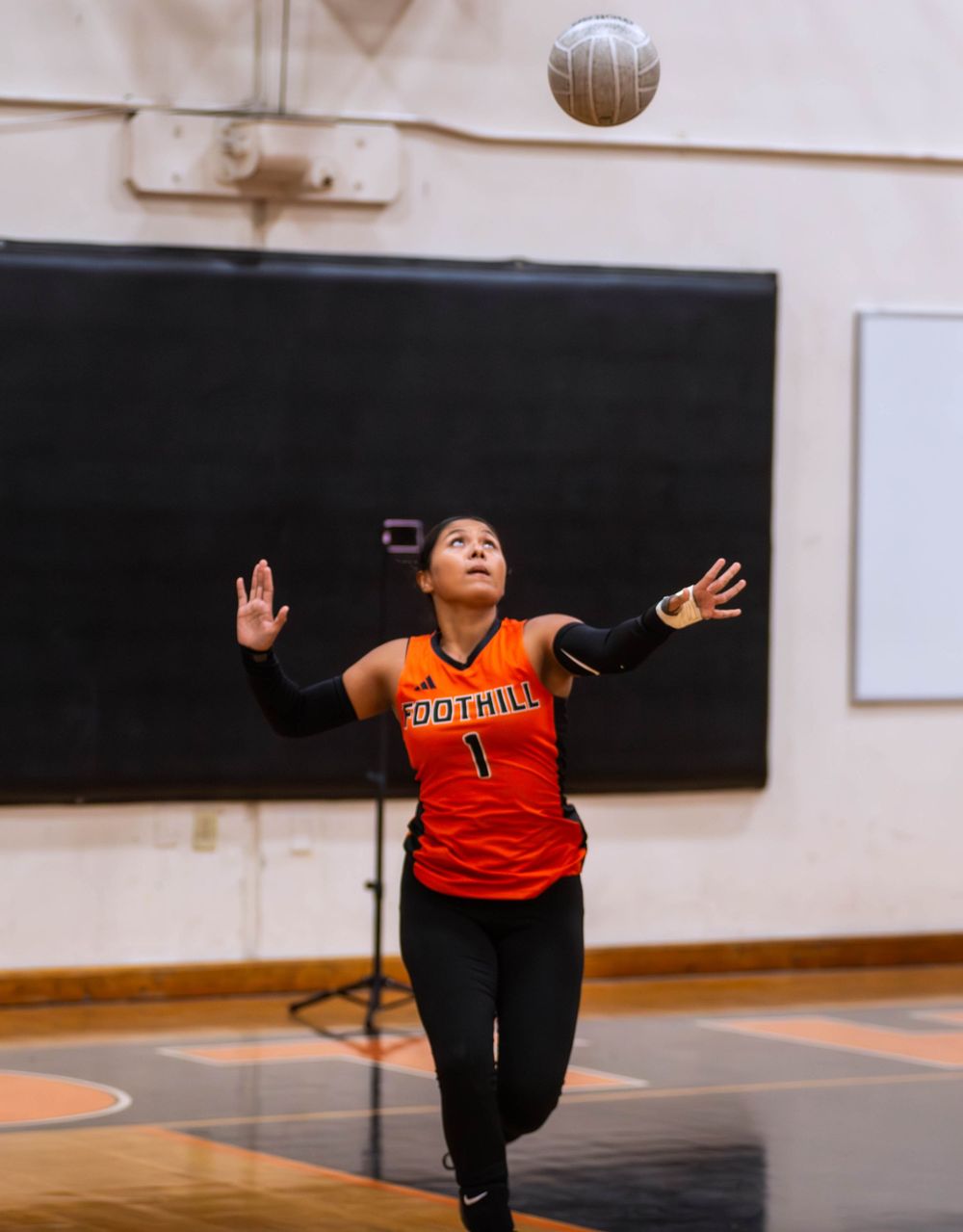 Volleyball player in orange jersey jumping to serve the ball during an indoor match.