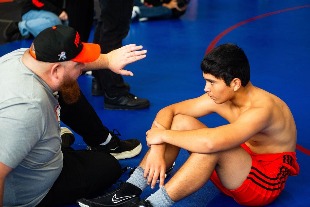 Two wrestlers engage in a competitive match on a blue wrestling mat during a training session.
