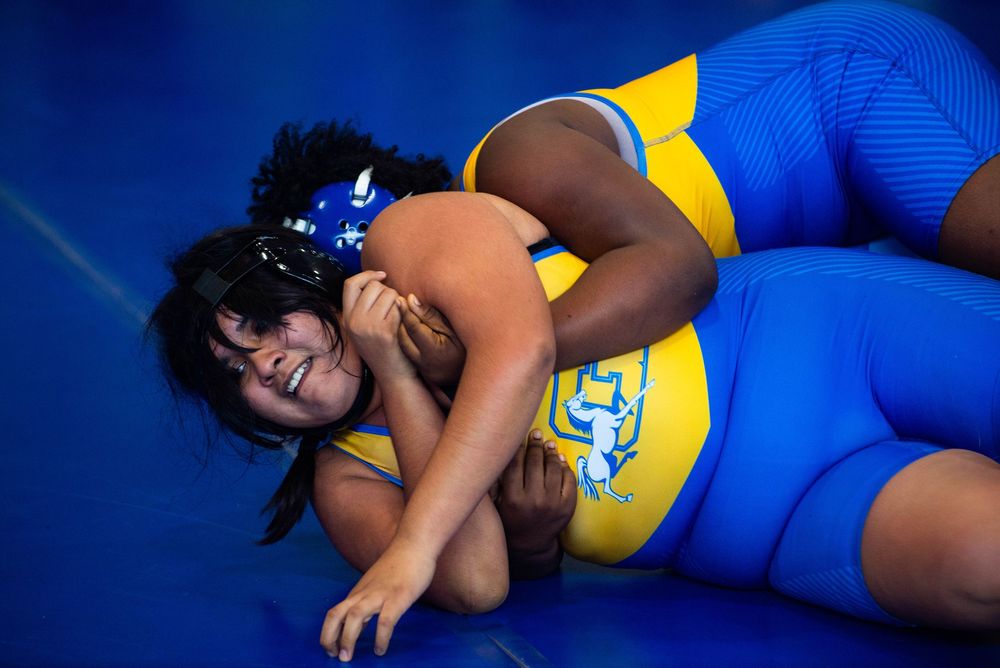 Two wrestlers compete on a blue mat wearing yellow and blue uniforms during an intense match.