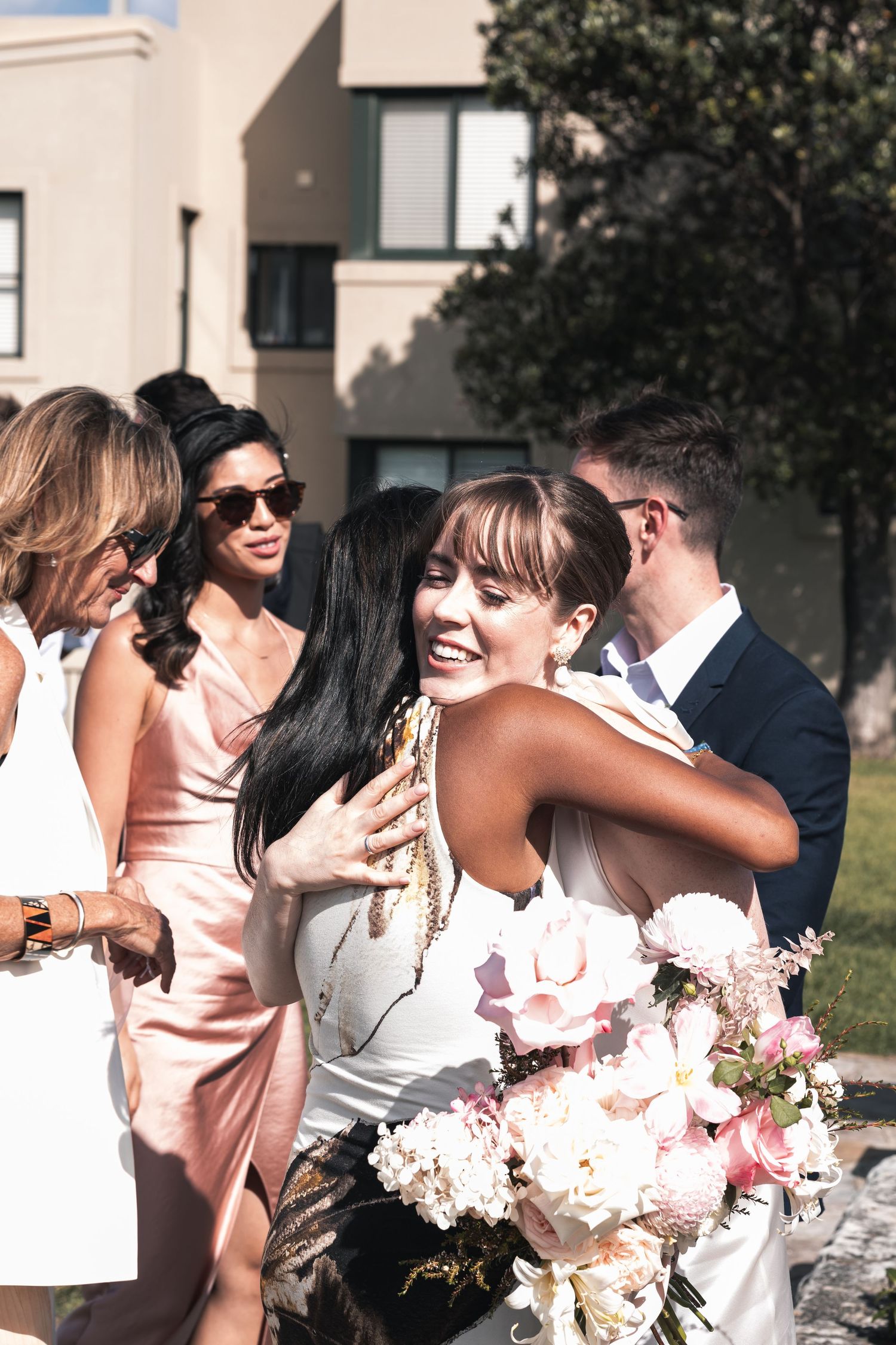 Wedding party gathers outdoors with bridesmaids in pink dresses and fresh floral bouquets.