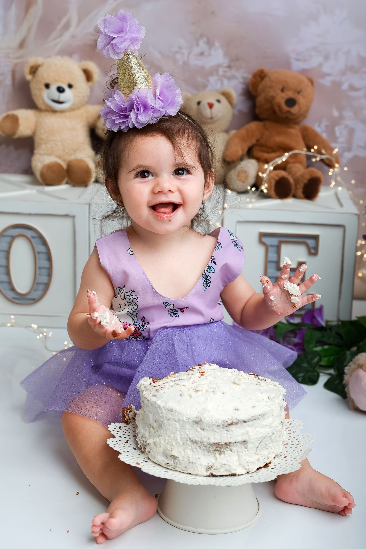 Birthday celebration with white cake, purple tutu dress, and teddy bears in the background.