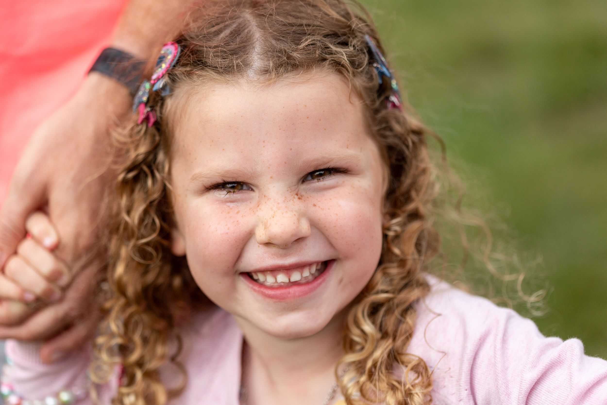 A cheerful expression captured in warm sunlight with curly hair and flower clips.