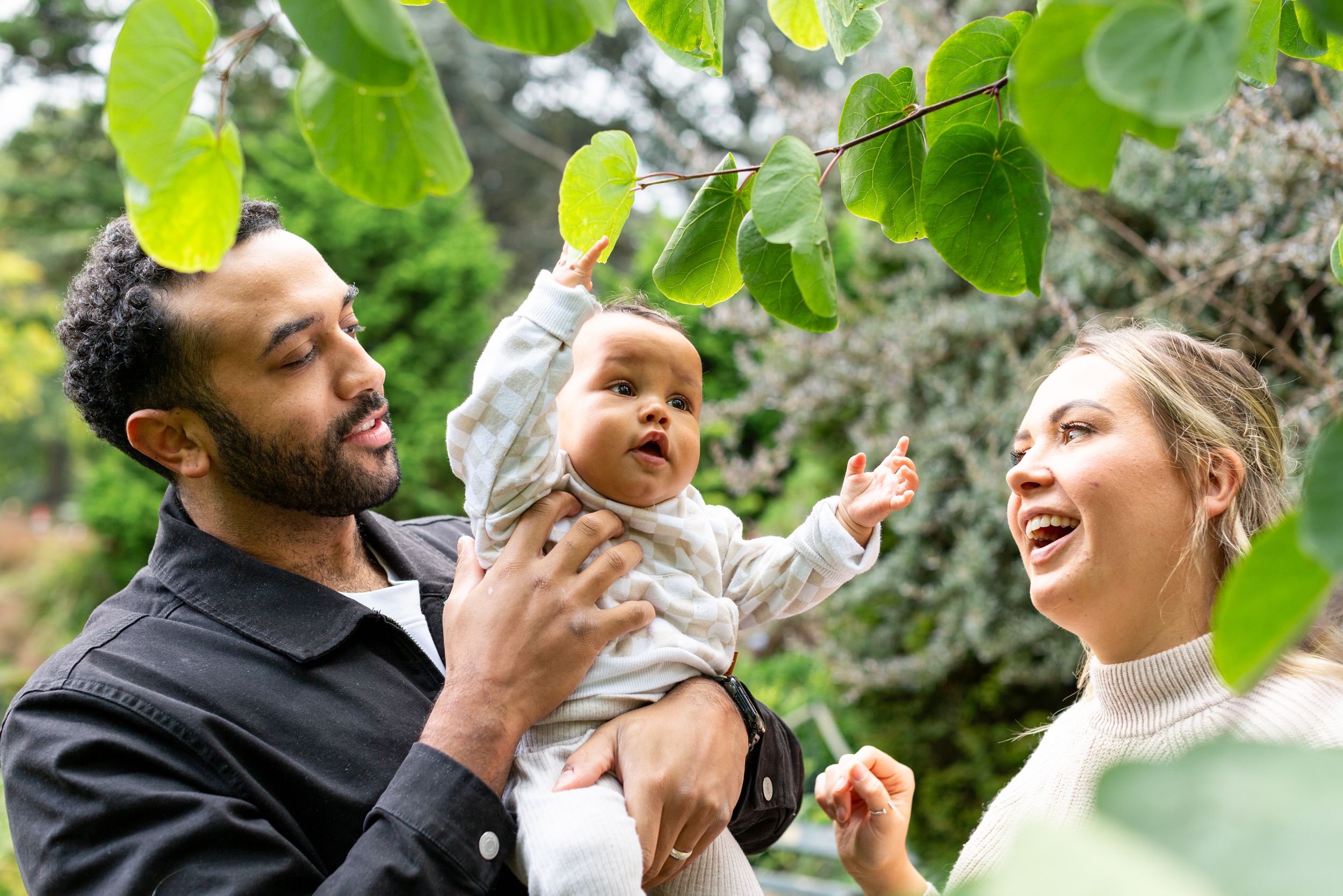 Family moment under green leaves with joyful expressions outdoors.