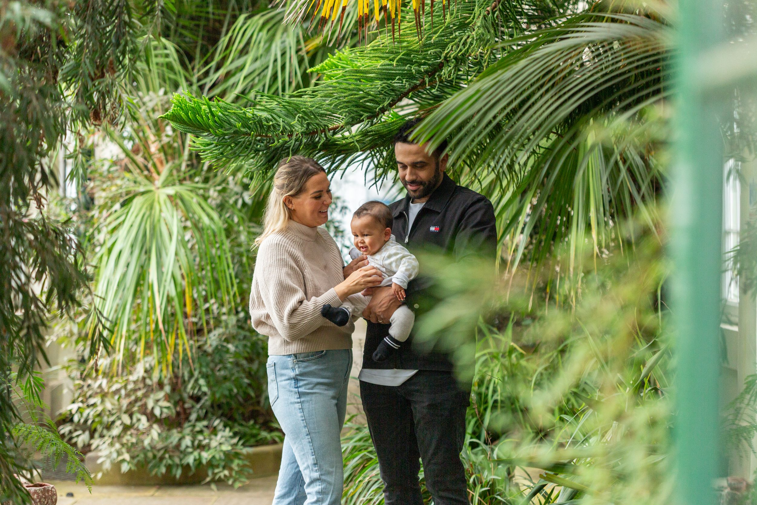 Family gathering among lush tropical plants in a greenhouse setting.