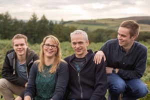 Group of four young adults sitting together outdoors on grassy hillside.