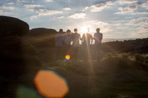 Group silhouetted against beautiful golden sunset on a hilltop with lens flare.