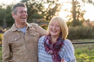 Couple laughing together outdoors during sunset in casual fall clothing.