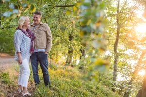 Couple standing together on grassy hill during golden sunset with trees in background.