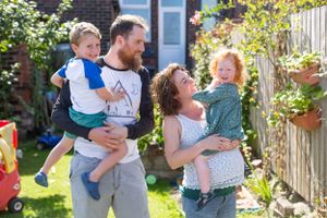 Family enjoying a fun moment together in a sunny backyard garden with blooming plants and flowers.