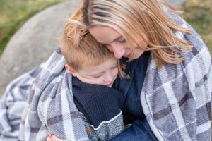 Tender moment captured between parent and child wrapped in plaid blanket outdoors.
