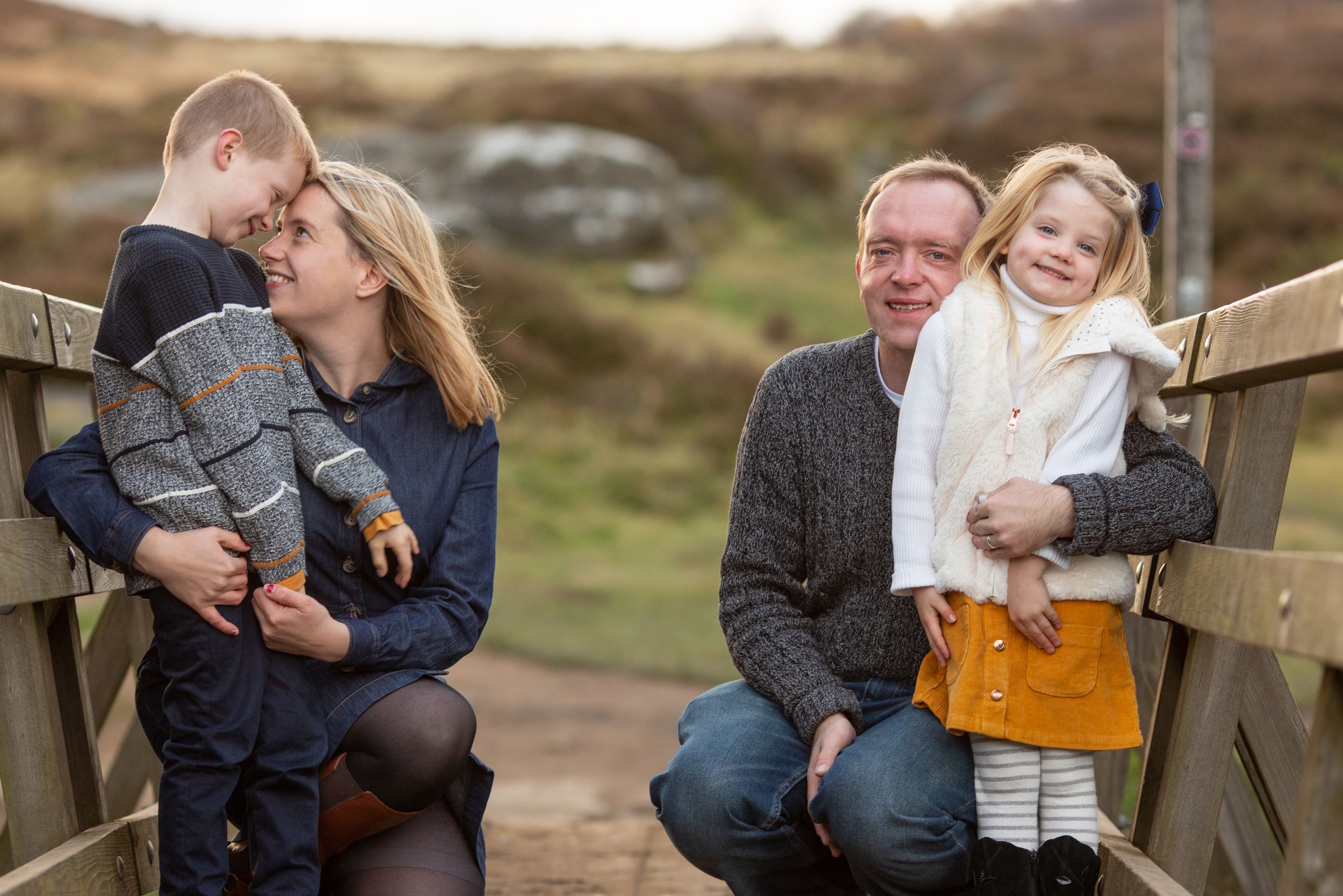 Family sharing intimate moments on wooden bridge during outdoor photo session.
