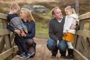 Casual family portrait on rustic wooden bridge with natural landscape background.