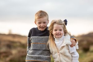 Two young children embrace and smile while wearing cozy sweaters outdoors.