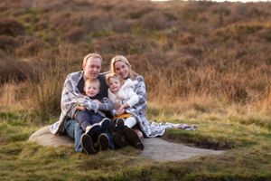 Family of four sitting together on rock outdoors in natural setting.