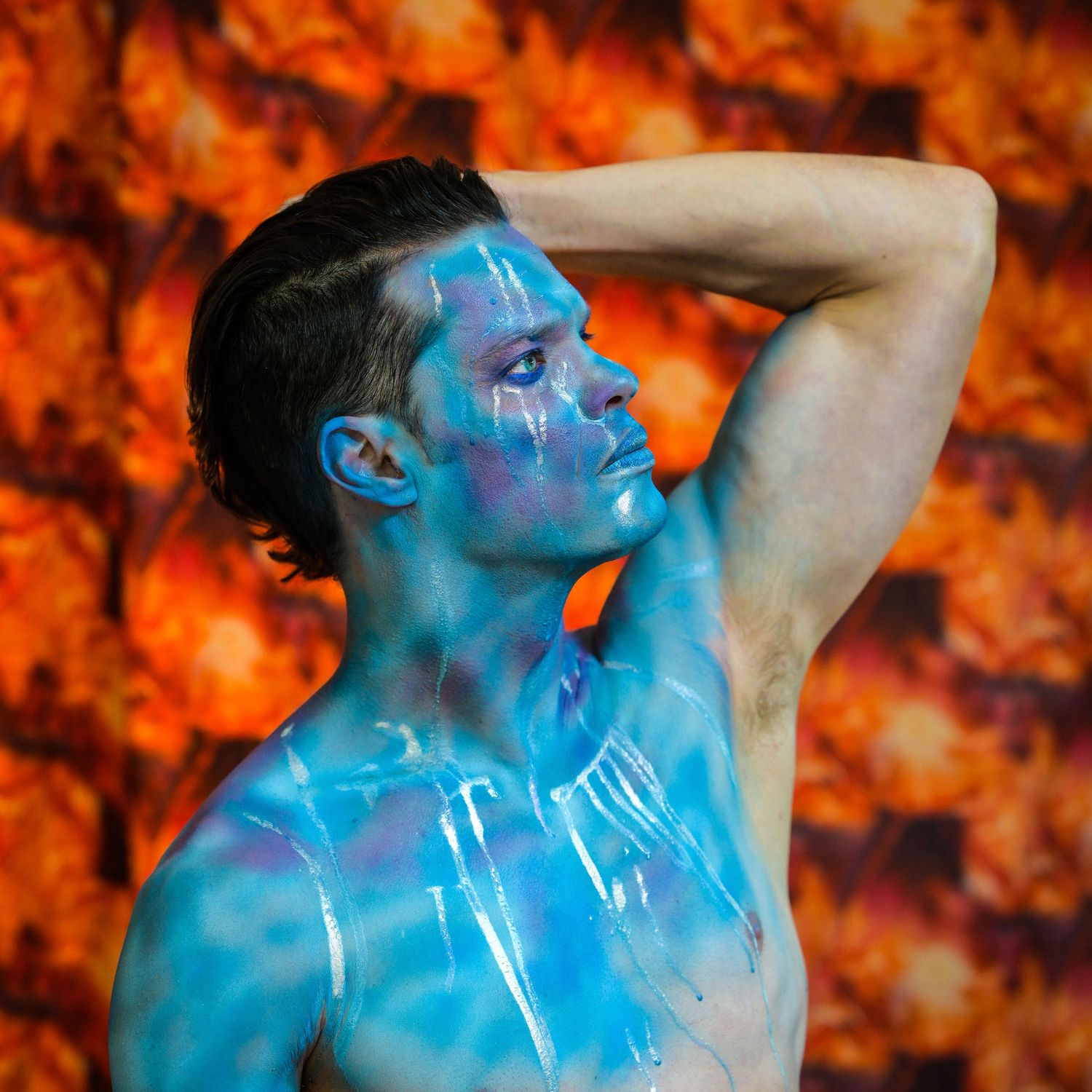 Creative portrait with blue body paint against orange autumn background.