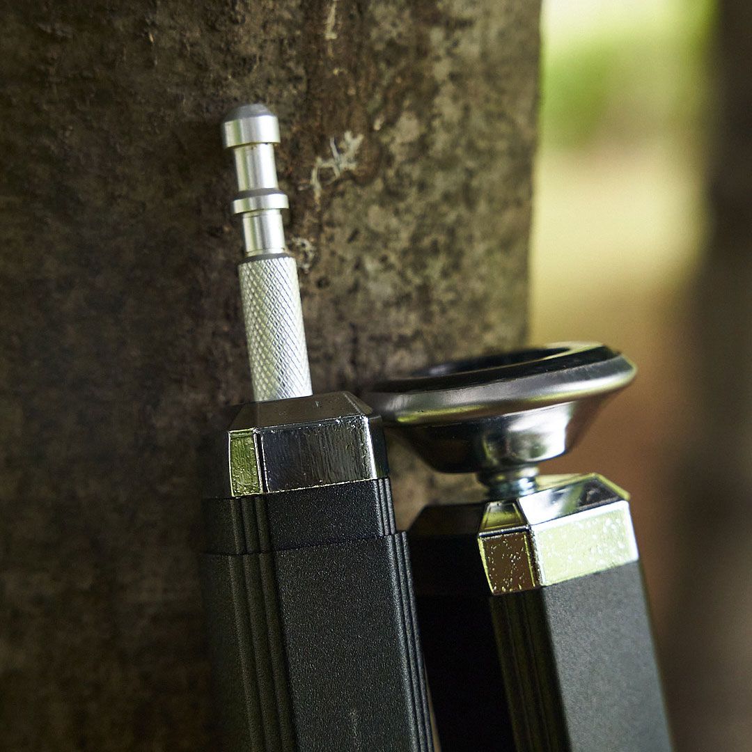Close-up of metallic connectors and components on a black device against a tree bark background.