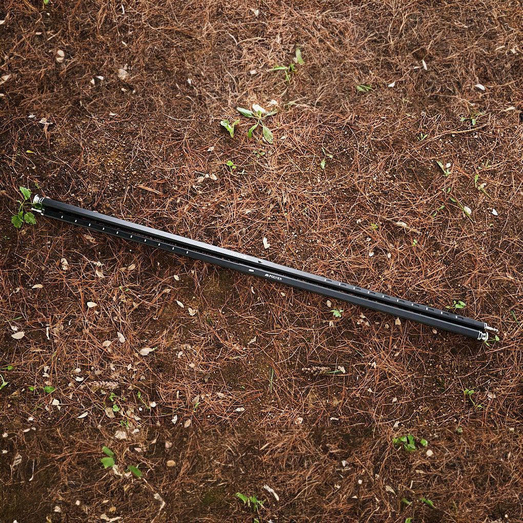 A black metal pole lying on brown soil with scattered leaves and small plants.