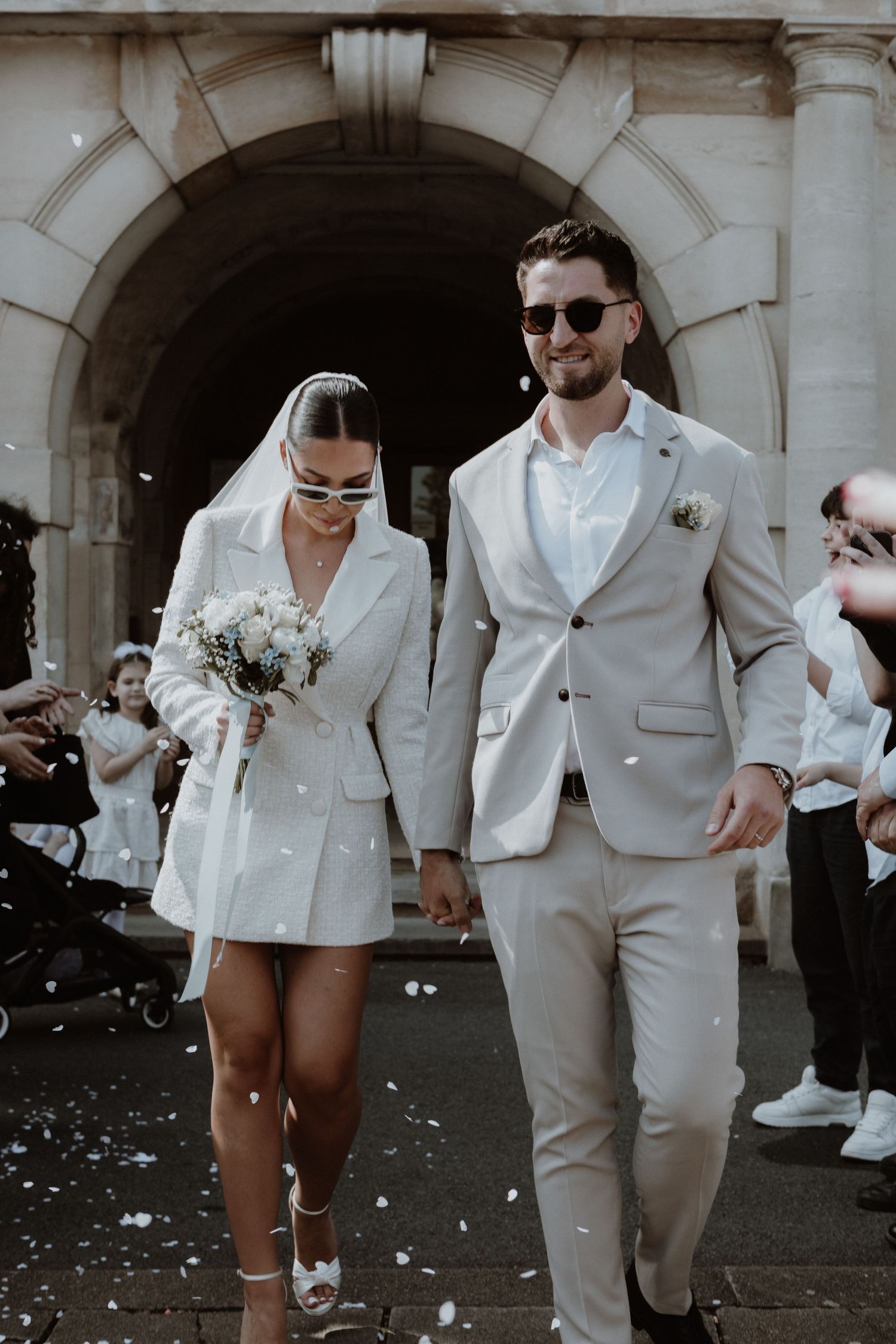 A modern bride in a short white blazer dress exits her ceremony with her groom.