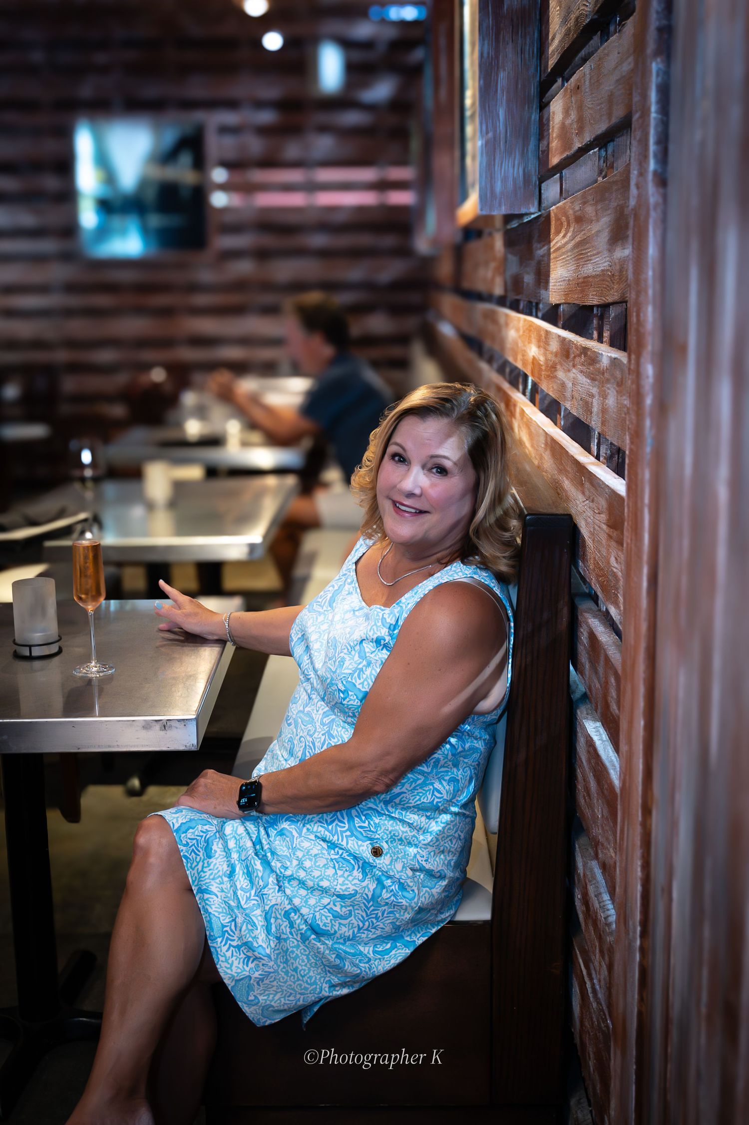Person in blue floral dress sitting at a rustic restaurant booth with wooden walls.