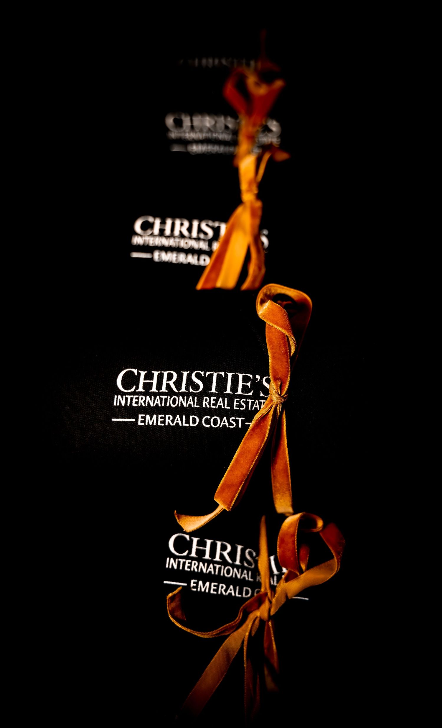 Christie's International Real Estate Emerald Coast branded gift bags with golden ribbons on dark background.