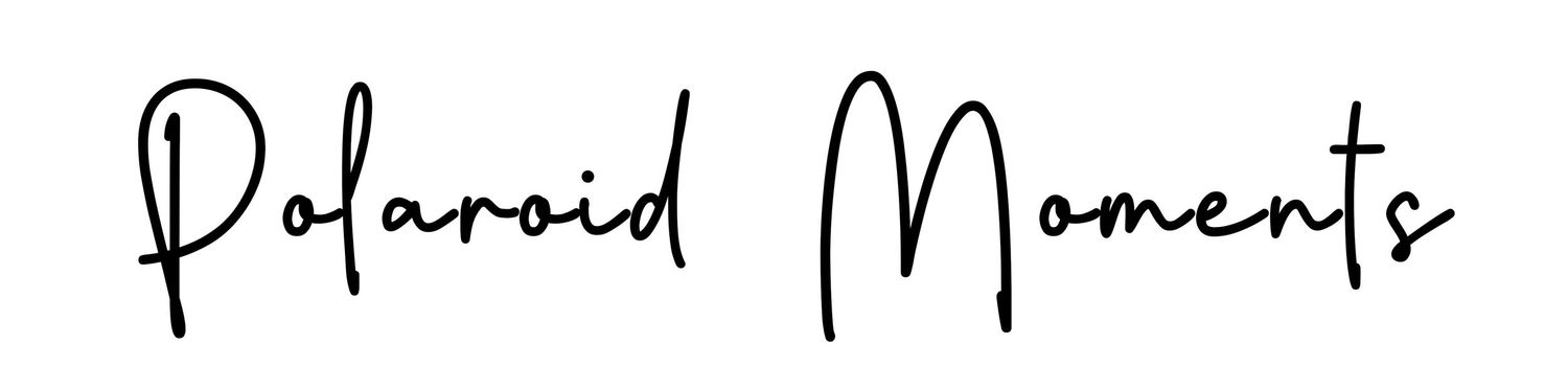 A polaroid camera sits on a wooden surface with text reading "Polaroid Moments" in cursive handwriting.