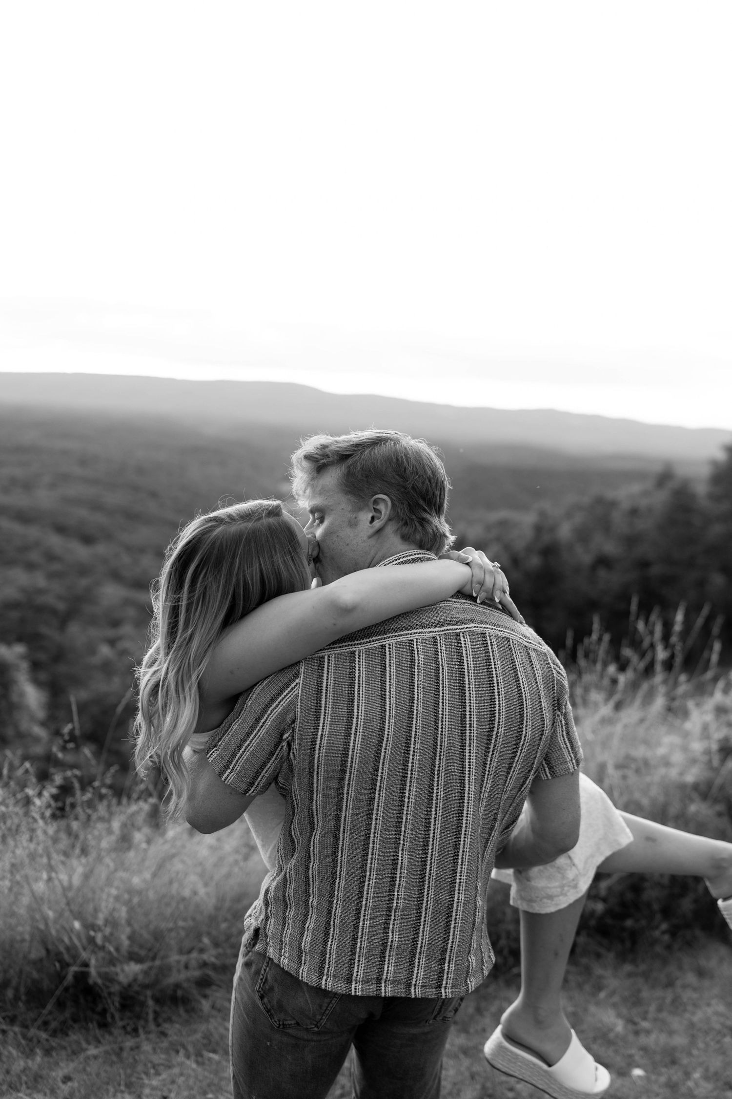 Black and white photo of a smiling couple sharing a tender moment in an outdoor field setting.