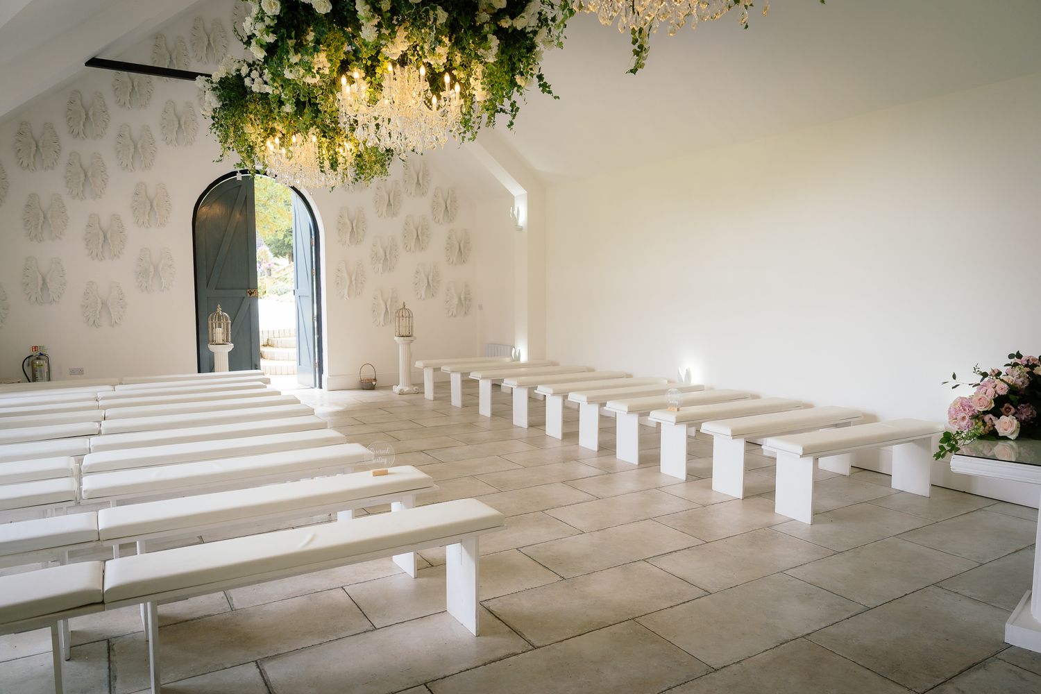 Elegant white chapel interior featuring stepped seating, arched windows, and hanging greenery. Woodhill Hall.