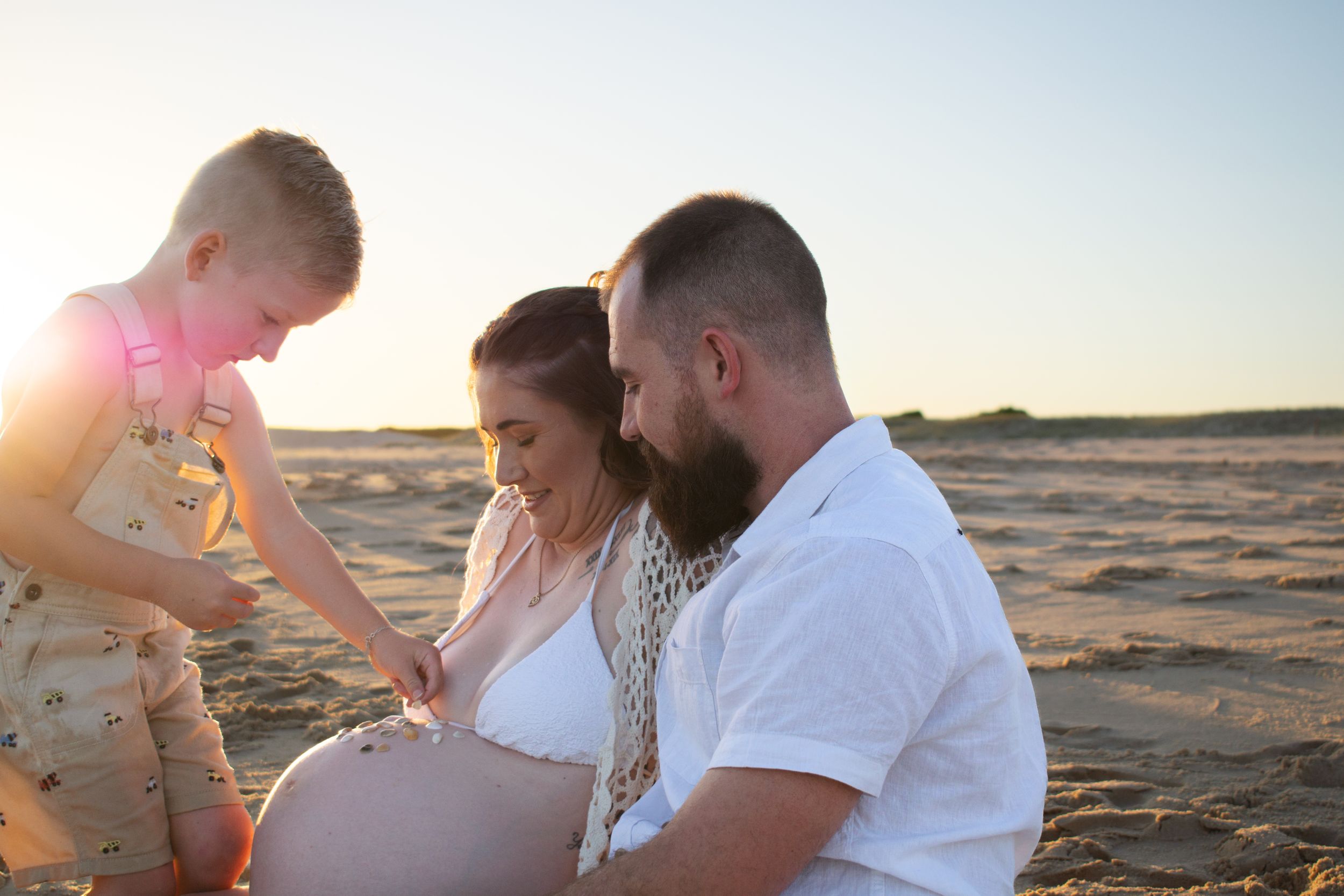 Newcastle maternity photographer capturing mother-to-be with husband and toddler at beach