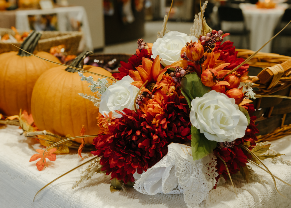 Fall wedding centerpiece with white roses, orange mums, and decorative pumpkins.