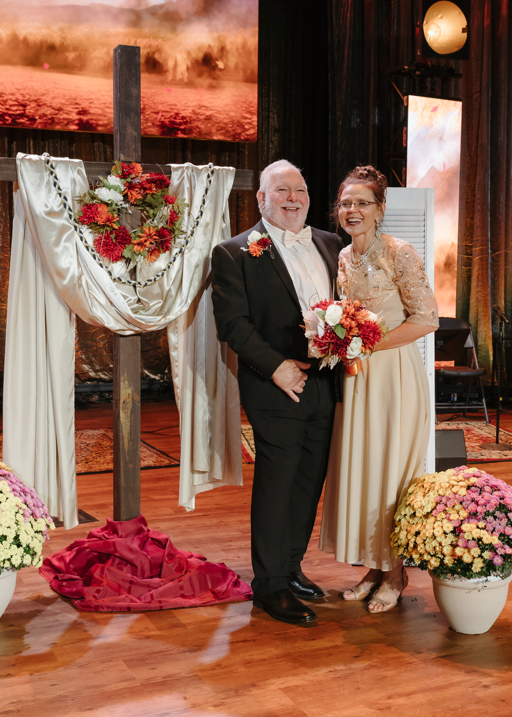 Bride and groom standing at altar with floral heart cross decoration at ceremony.