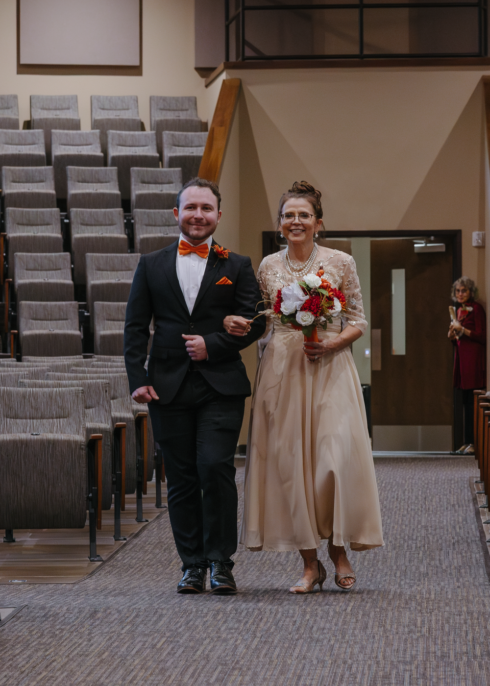Bride walking down church aisle escorted by groomsman holding fall bouquet.