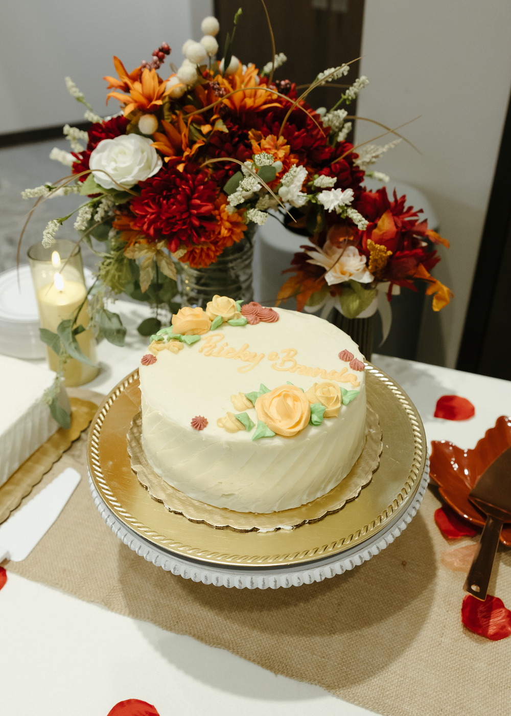 Elegant white wedding cake decorated with peach roses on gold stand, surrounded by autumn floral arrangement.