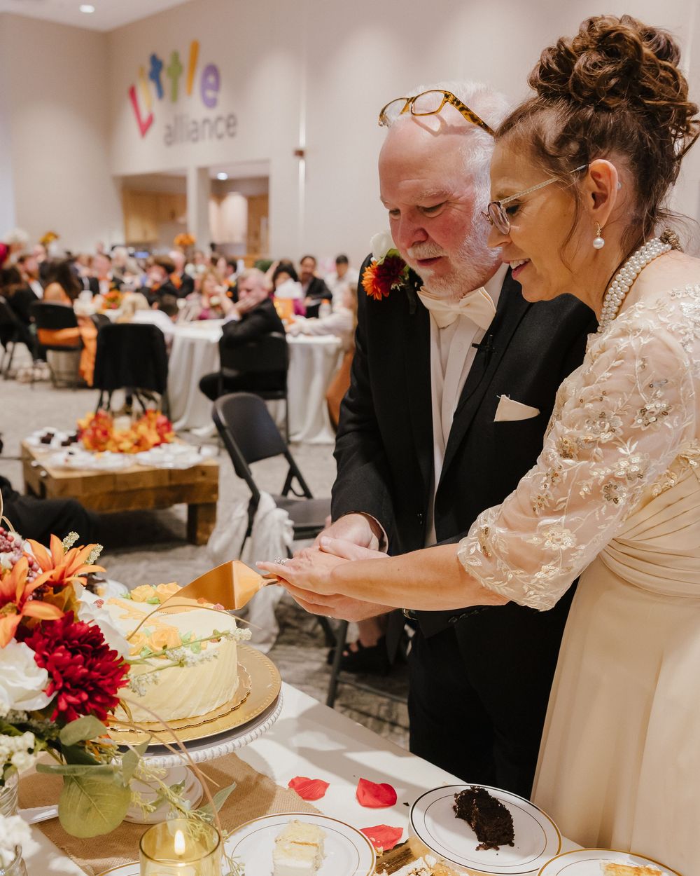 Bride and groom cutting wedding cake at elegant fall-themed reception venue.