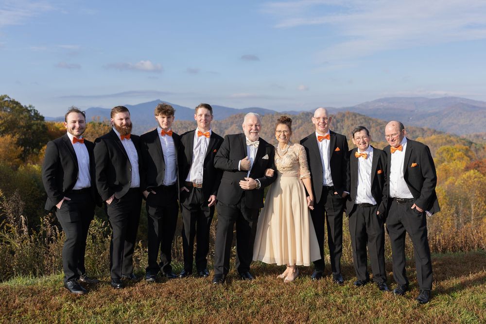 Wedding party posing with bride and groom against stunning mountain backdrop in autumn.
