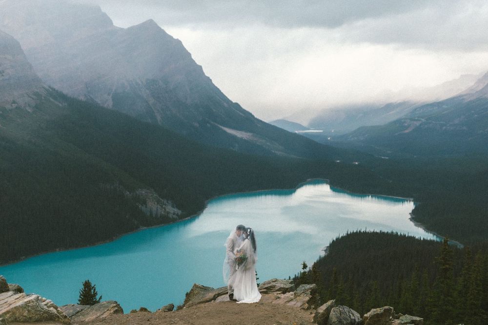 bride and groom hold each other with a wide view over Peyto Lake and surrounding mountains in Banff National Park