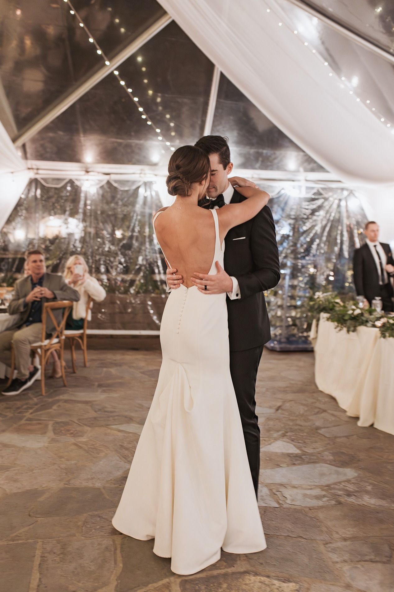 A couple shares their first dance at a wedding reception under a white tent with twinkling lights and stone flooring at Lake Oak Meadows.