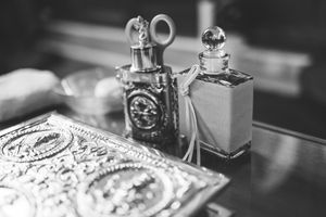 Black and white close-up photography of vintage perfume bottles and ornate vanity accessories on an elegant dressing table.