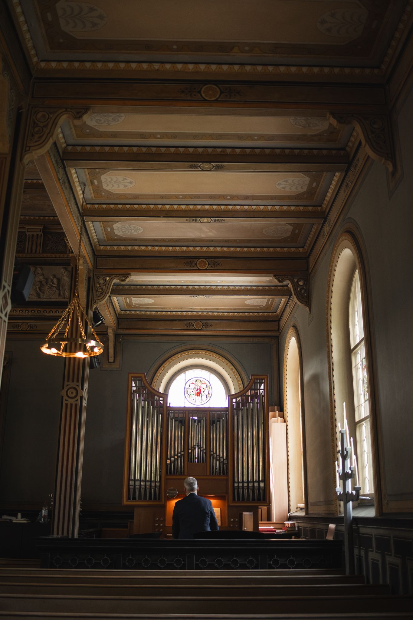 Dark church interior with arched windows and organ pipes illuminated by natural light from the side.