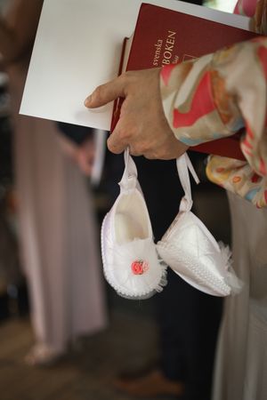 Close-up view of hands holding delicate white baby shoes with pink ribbons.