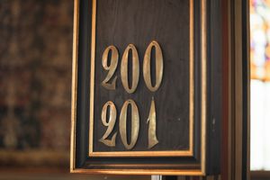 Vintage hotel room numbers in gold frames mounted on dark wooden wall panels.
