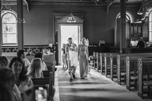 A black and white photo of a church interior during a wedding ceremony with light streaming through stained glass windows.