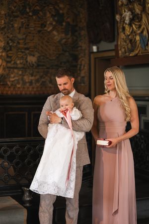 A family shares a tender moment during a christening ceremony, with the baby wearing a white lace gown.