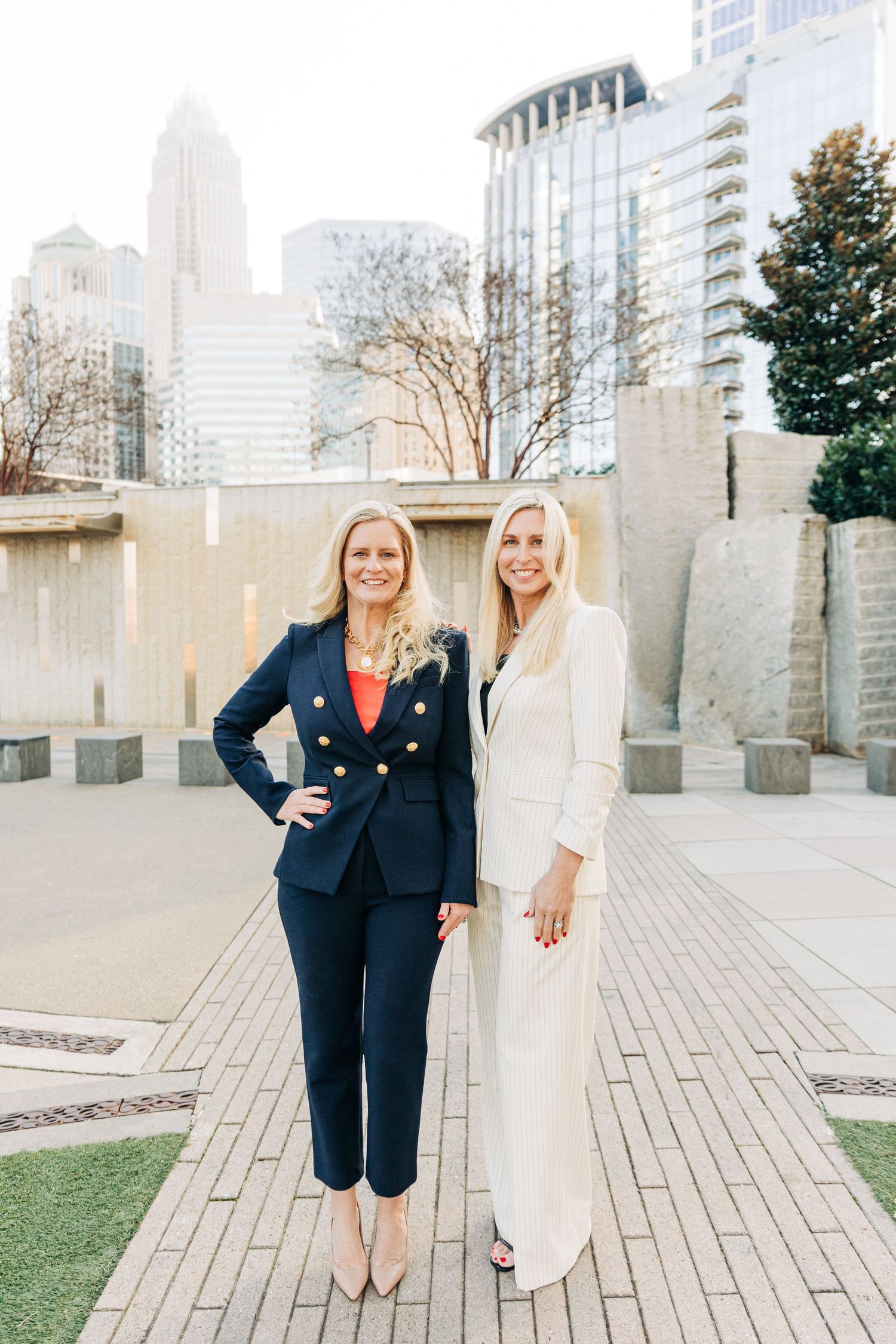 Two people in contrasting outfits, one in a navy suit and one in white, pose together in uptown Charlotte for headshots