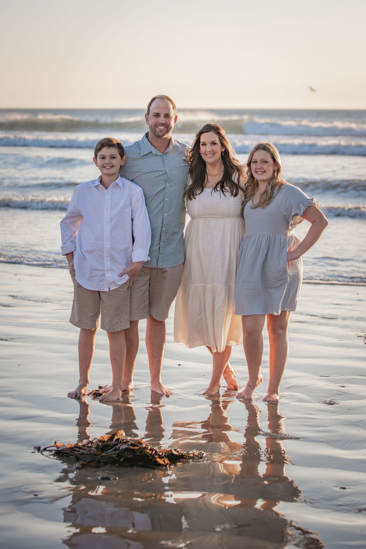 Family standing together at sunset on a beach with gentle waves in the background.